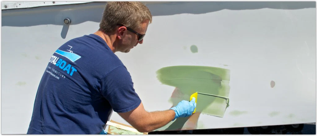 Man in TotalBoat shirt applying epoxy fairing compound to boat hull with yellow spreader