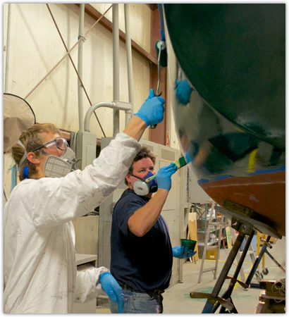Two men applying topside paint to boat hull with roller and brush