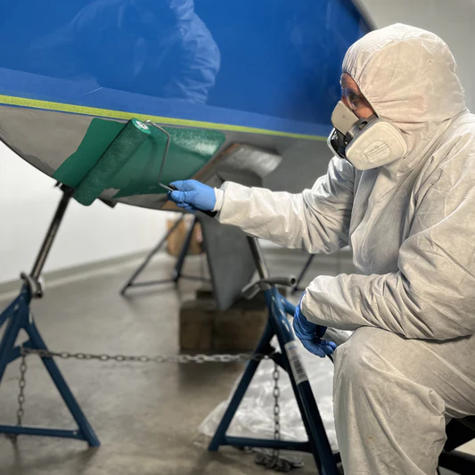 Person in paint suit and respirator applying TotalBoat Spartan in green with roller on boat
