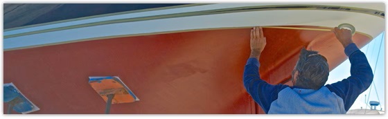 Man applying masking tape to boat hull to prepare for bottom painting