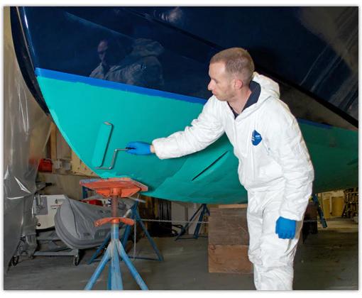 Man wearing paint suit applying paint on boat bottom with roller