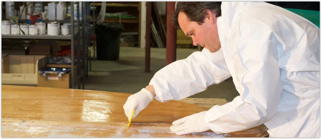 Man in paint suit applying epoxy resin to fiberglass on wooden boat