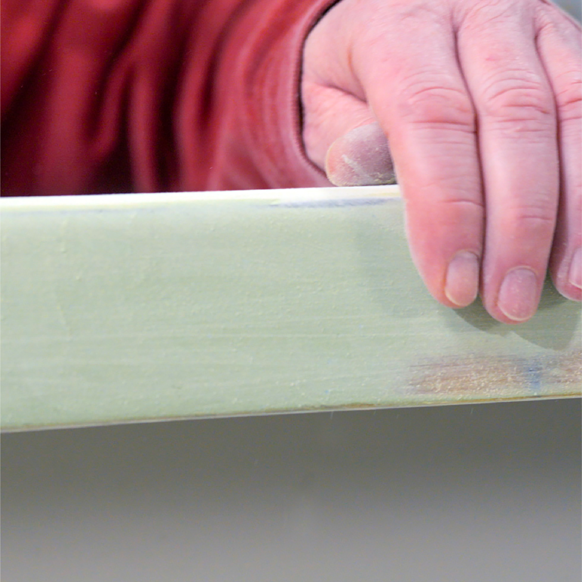 Close up of cured epoxy fairing compound on boat hull with man's hand in view