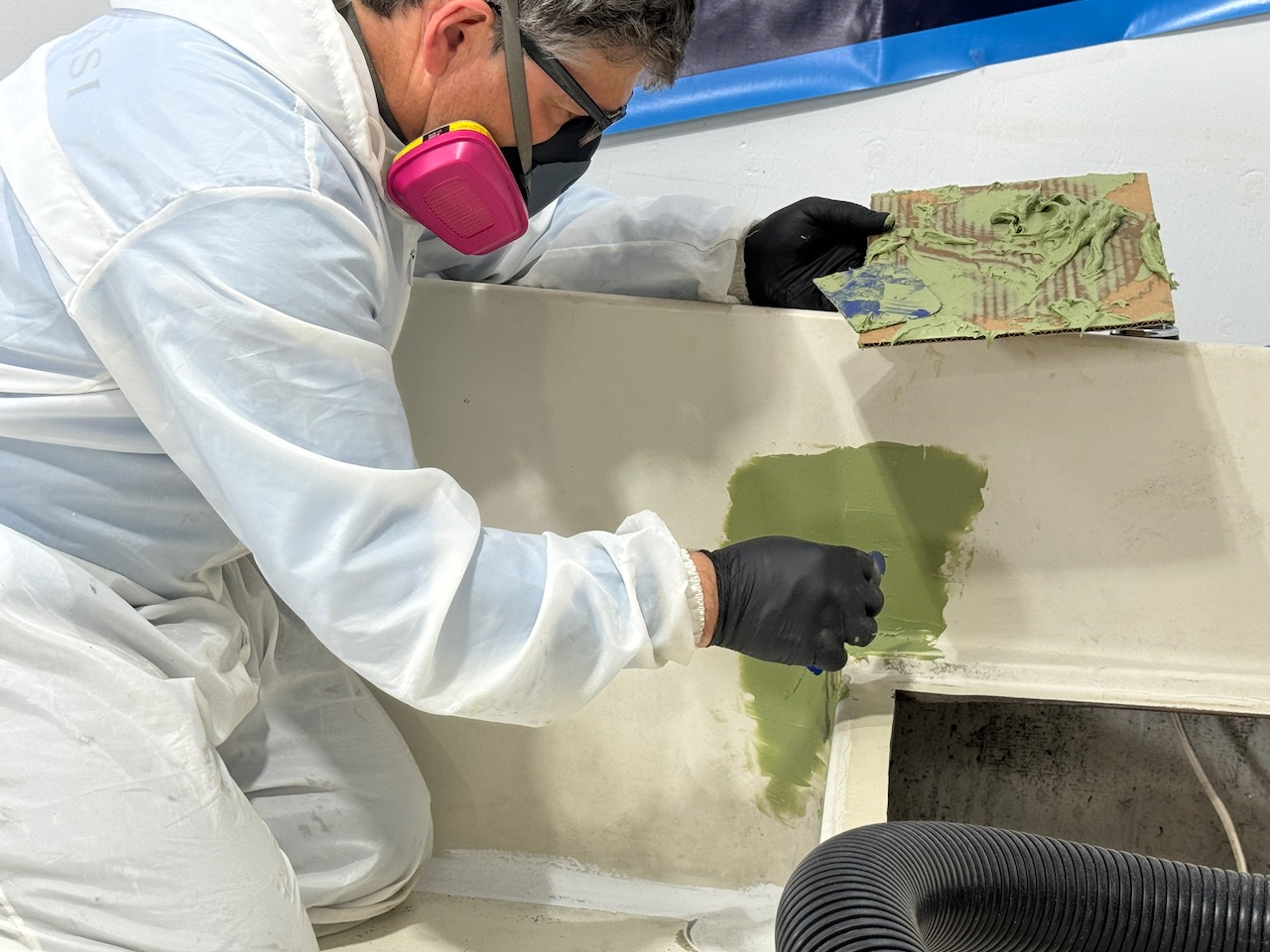 Man wearing protective equipment while applying TotalBoat TotalFair fairing compound on boat