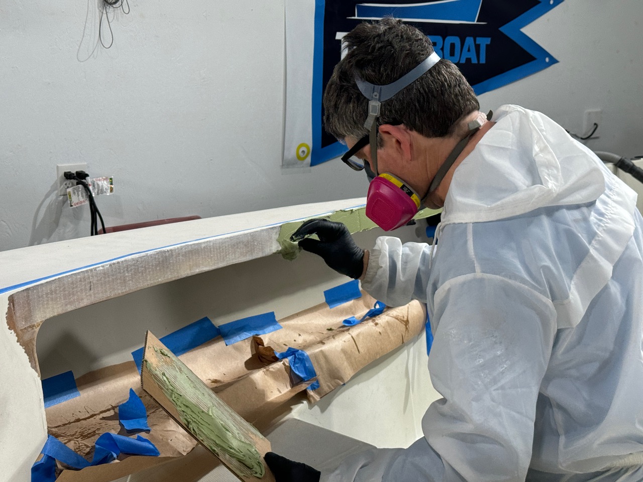 Man applying TotalBoat TotalFair epoxy fairing compound on boat hull with masking tape