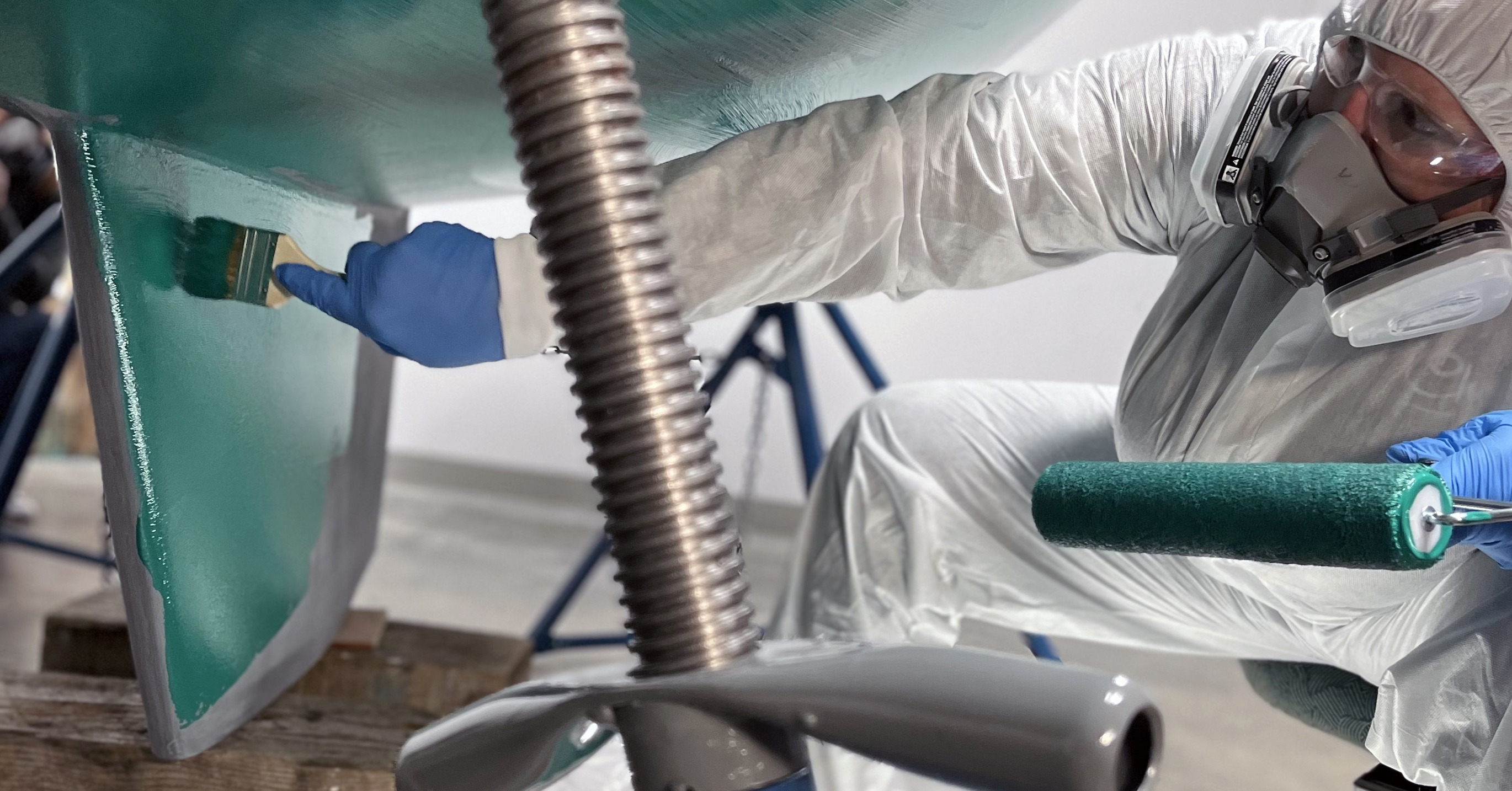 Person in protective equipment applying TotalBoat Spartan paint on boat bottom