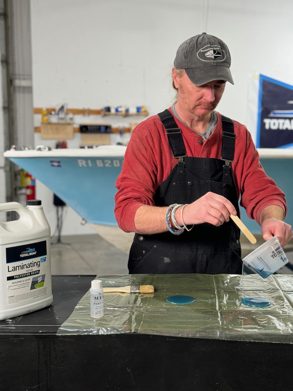 Man in red shirt applying TotalBoat Polyester Laminating Resin in layup